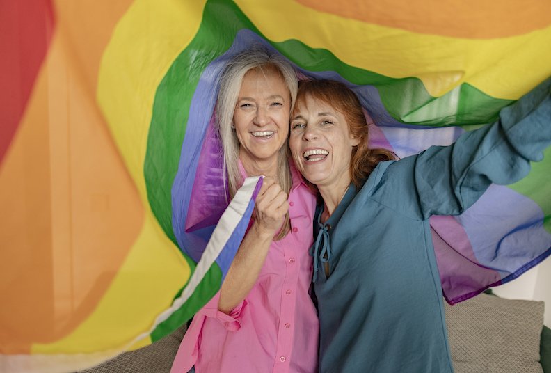 two women hoist the gay rainbow flag. I support the lgbti, gay, homosexual, bisexual, lesbian, trans, non-binary community. Fight for freedom and rights